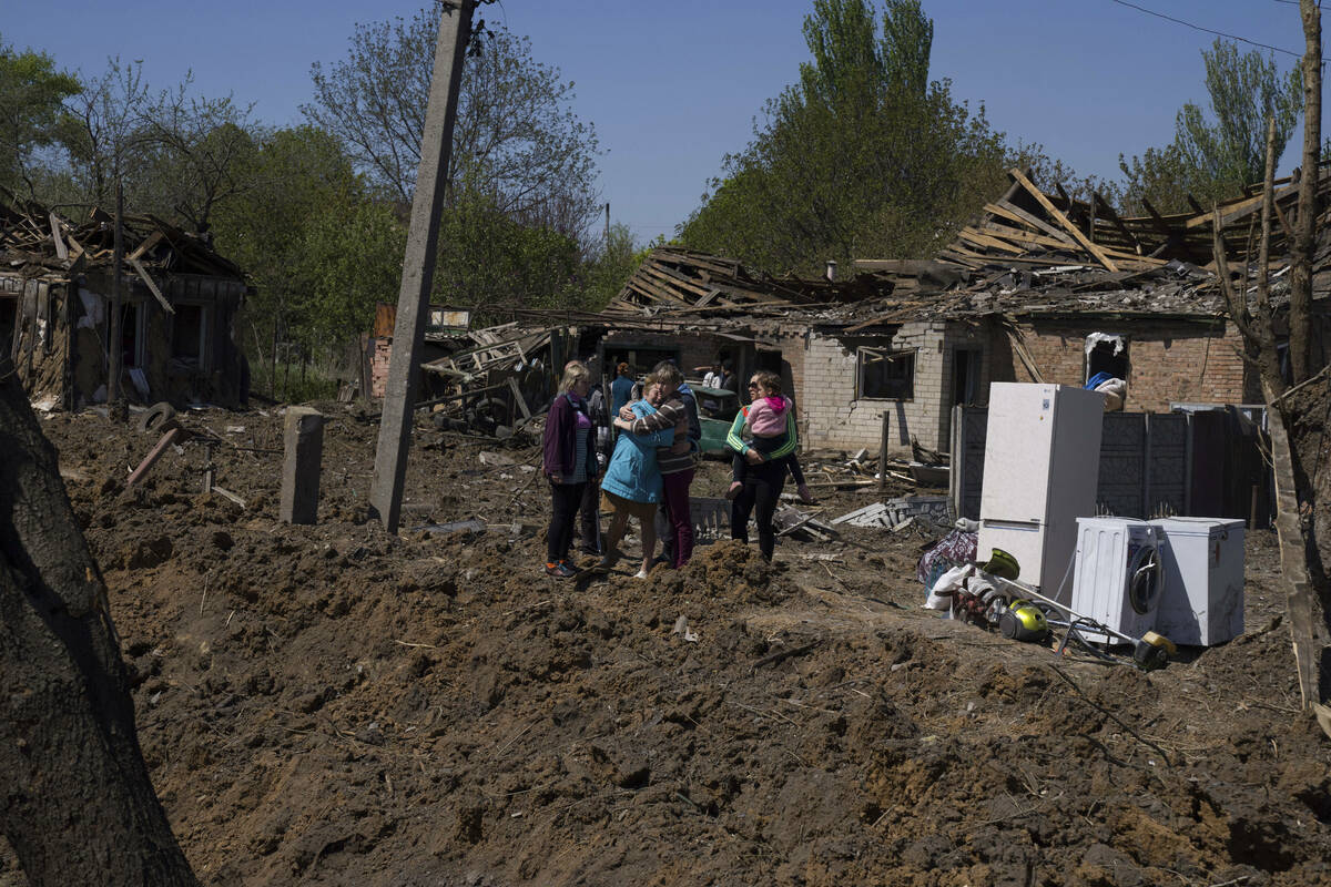 People react as they stand next to a crater in destroyed residential area after Russian airstri ...