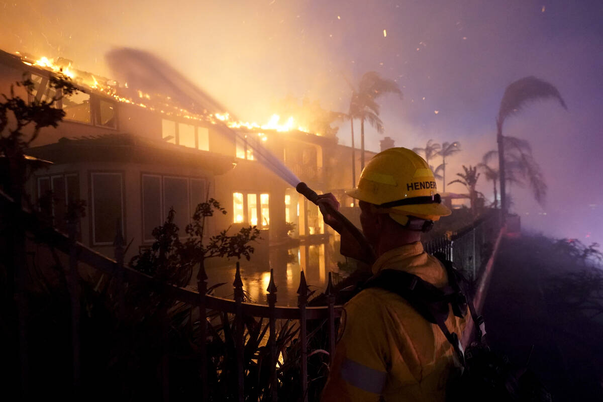 A firefighter works to put at a structure burning during a wildfire Wednesday, May 11, 2022, in ...