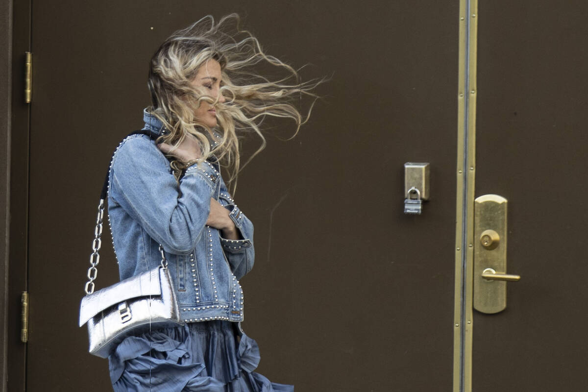 A pedestrian has her hair blown by strong wind as she walks along Main Street in downtown on Fr ...