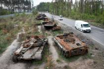 FILE - Cars pass by destroyed Russian tanks in a recent battle against Ukrainians in the villag ...