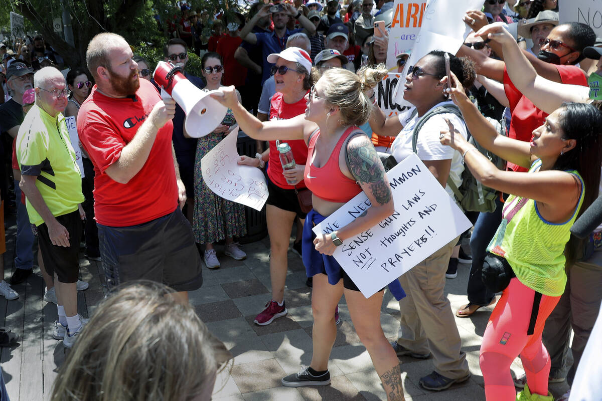 A counter-protester, left in red, is shouted down and has his megaphone taken away by rally att ...