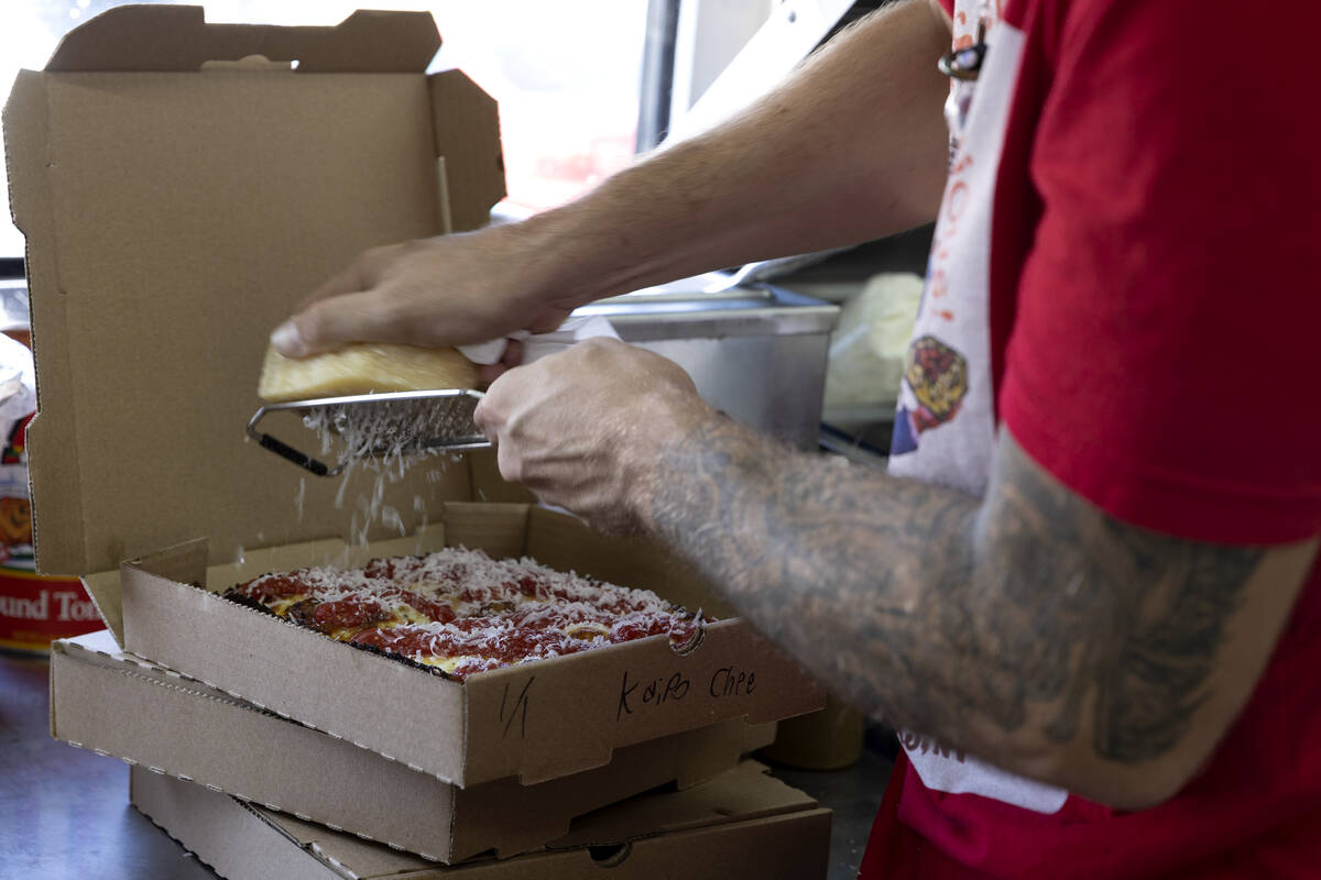 Chris Hill grates fresh parmesan over a Detroit-style pizza at Izzy’s Pizza Bus outside ...