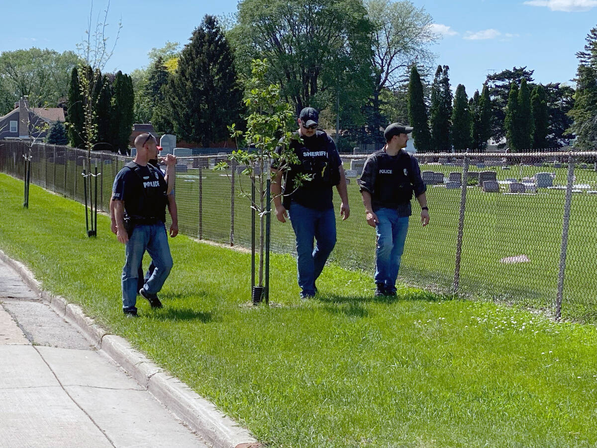 Four law enforcement officers walk along the fence that borders Graceland Cemetery after shooti ...