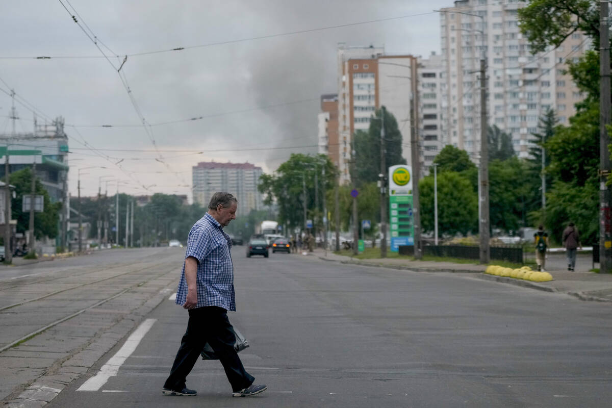 A man crosses a street as smoke rises in the background after Russian missile strikes in Kyiv, ...