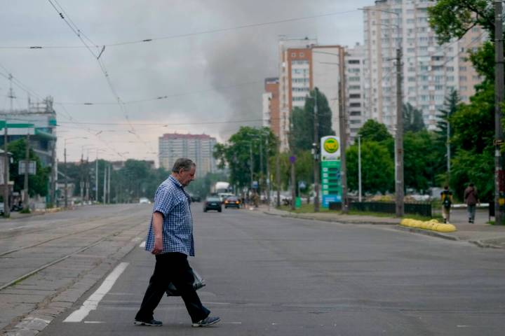 A man crosses a street as smoke rises in the background after Russian missile strikes in Kyiv, ...