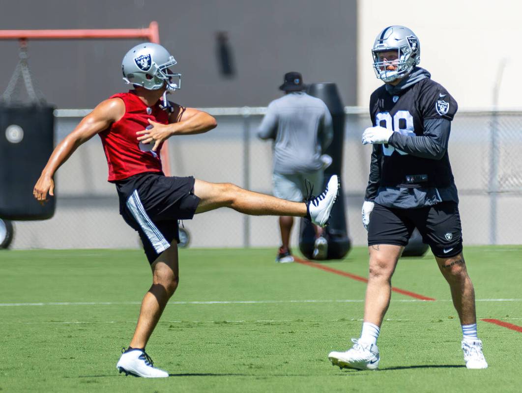 Raiders quarterback Derek Carr (4, left) throws a kick as teammate defensive end Maxx Crosby (9 ...