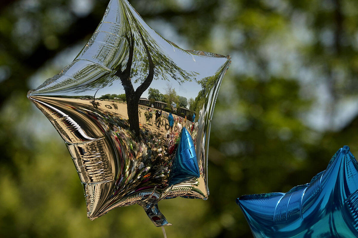 Mourners are reflected in a balloon at a memorial outside Robb Elementary School created to hon ...