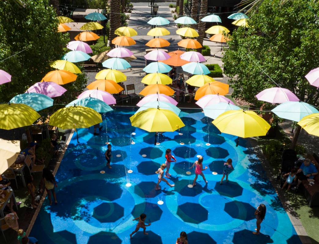 Small umbrellas are hung over a splash pad as children cool themselves at The District on Thurs ...