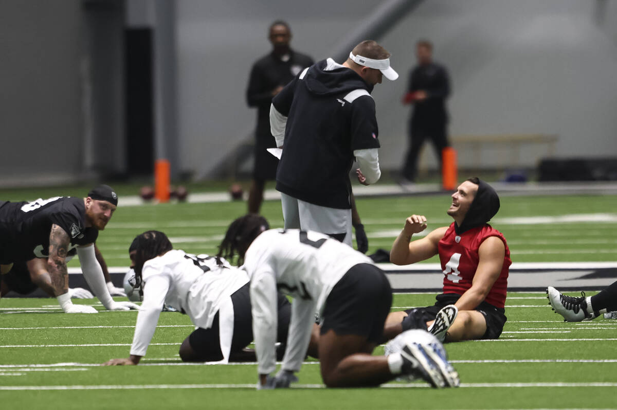 Raiders head coach Josh McDaniels talks with quarterback Derek Carr as players stretch during m ...