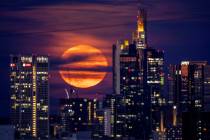 The full moon rises behind buildings in the banking district in Frankfurt, Germany, late Tuesda ...