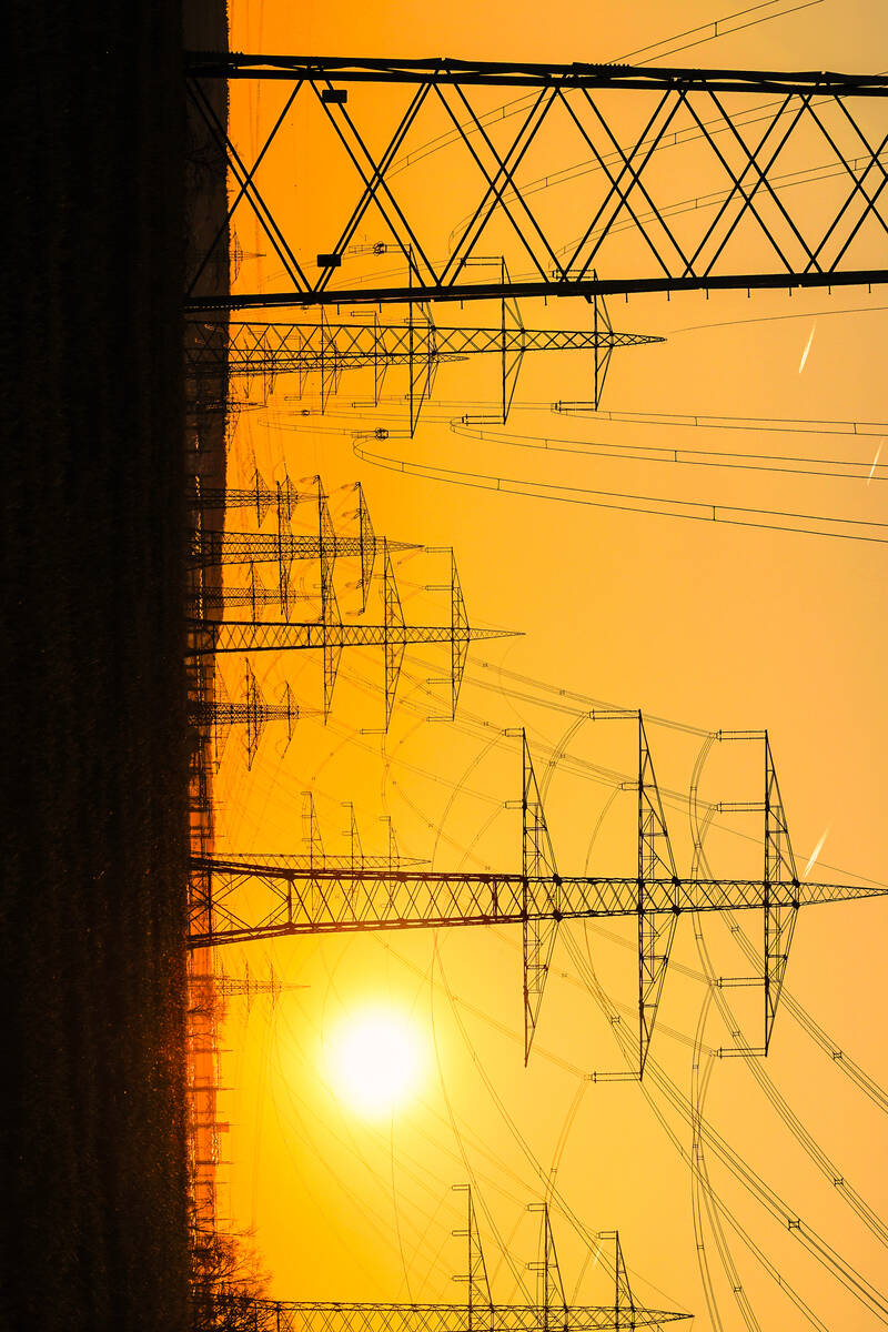 Electricity poles and electric power transmission lines against vibrant orange sky at sunset on ...