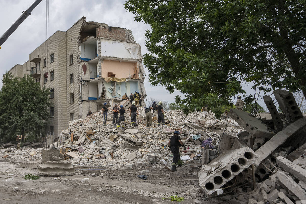 Rescue workers stand on the rubble at the scene in the after math of a missile strike that his ...