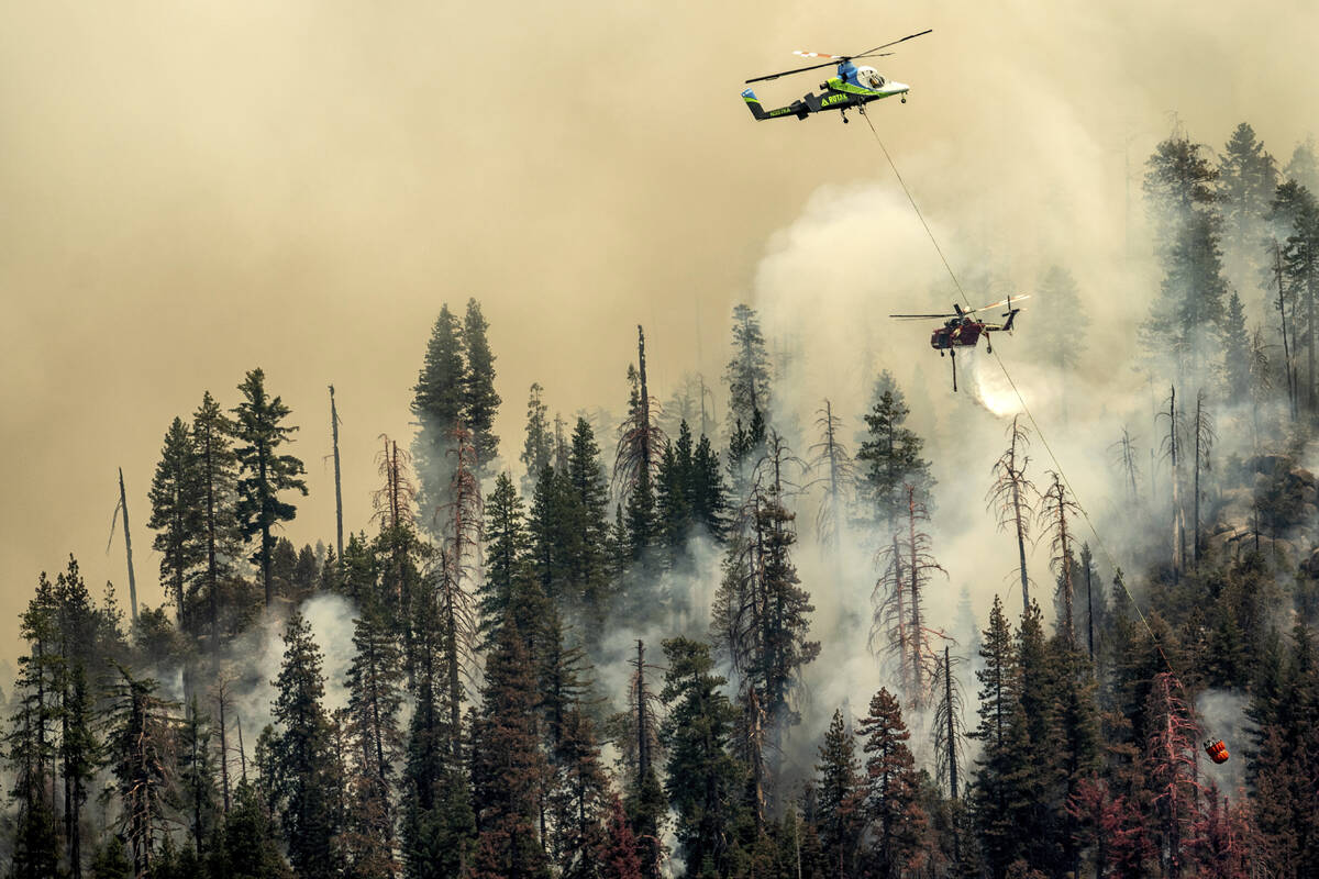 Seen from unincorporated Mariposa County, Calif., a helicopter drops water on the Washburn Fire ...