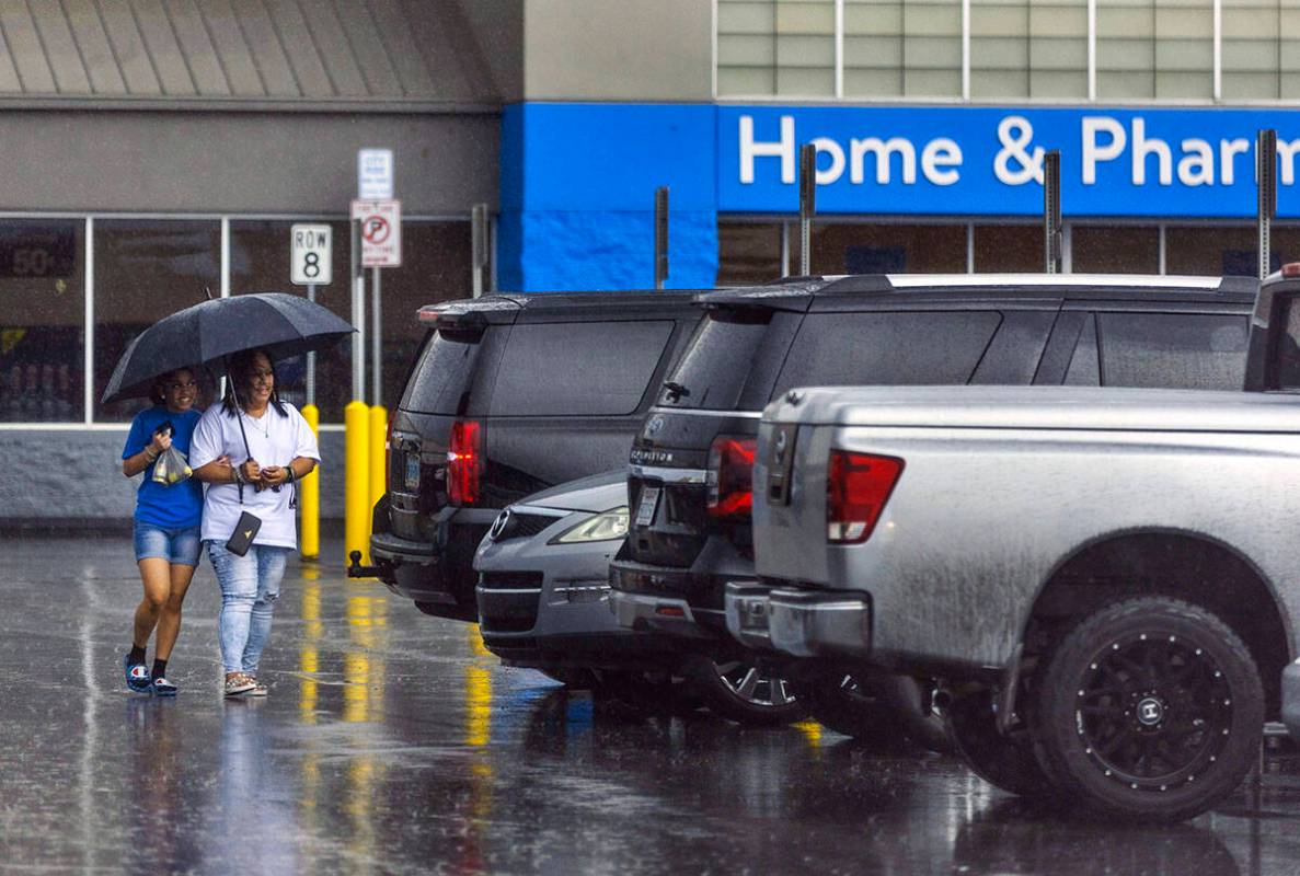 Shoppers take cover beneath an umbrella in a Walmart parking lot as rain moves through the vall ...