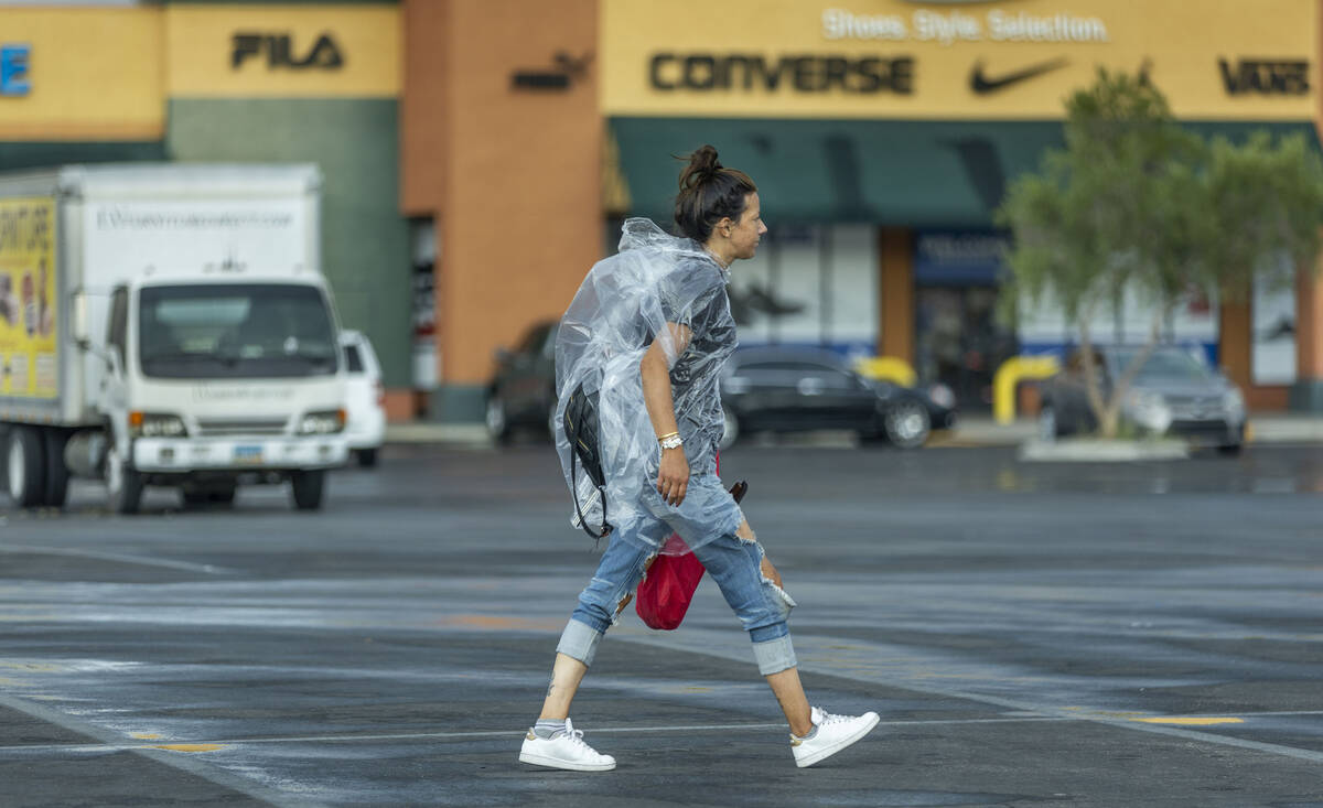 A shopper in a plastic raincoat walks through a Walmart parking lot as rain moves through the v ...