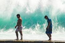 People walk in front of the high surf near Kapahulu Groin (Waikiki Wall) in Waikiki, Hawaii, Su ...