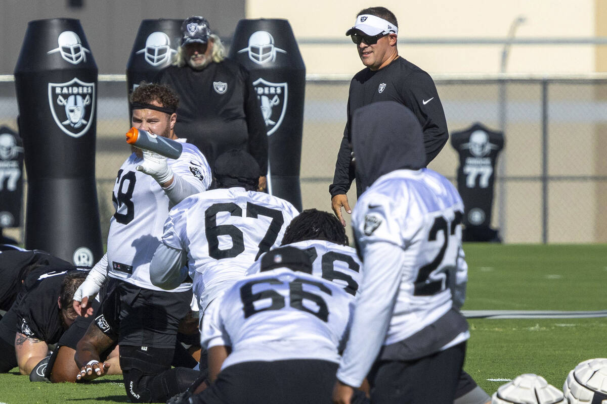 Raiders head coach Josh McDaniels, right, walks through as offensive linemen’s warm ups ...