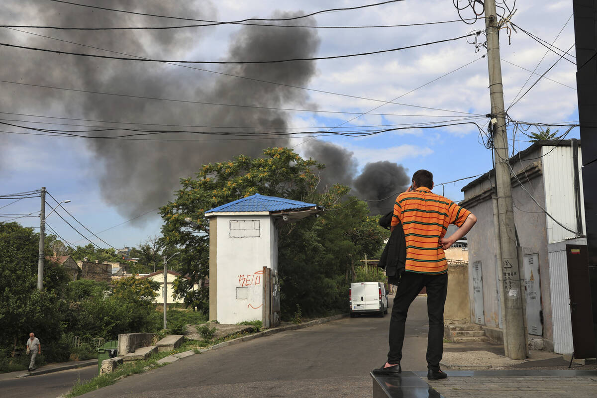 A man talks on a phone as smoke rises in the air after shelling in Odesa, Ukraine, Saturday, Ju ...