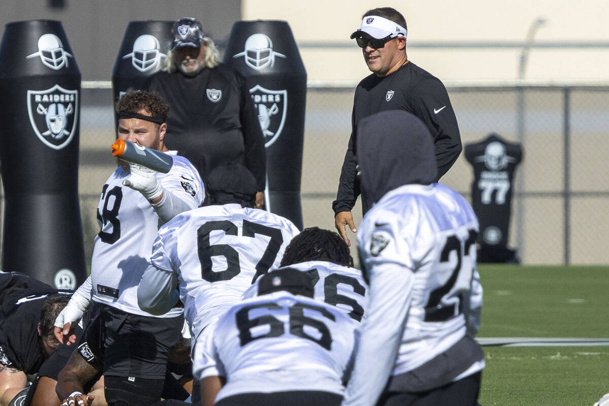 Raiders head coach Josh McDaniels, right, walks through as offensive linemen’s warm ups ...