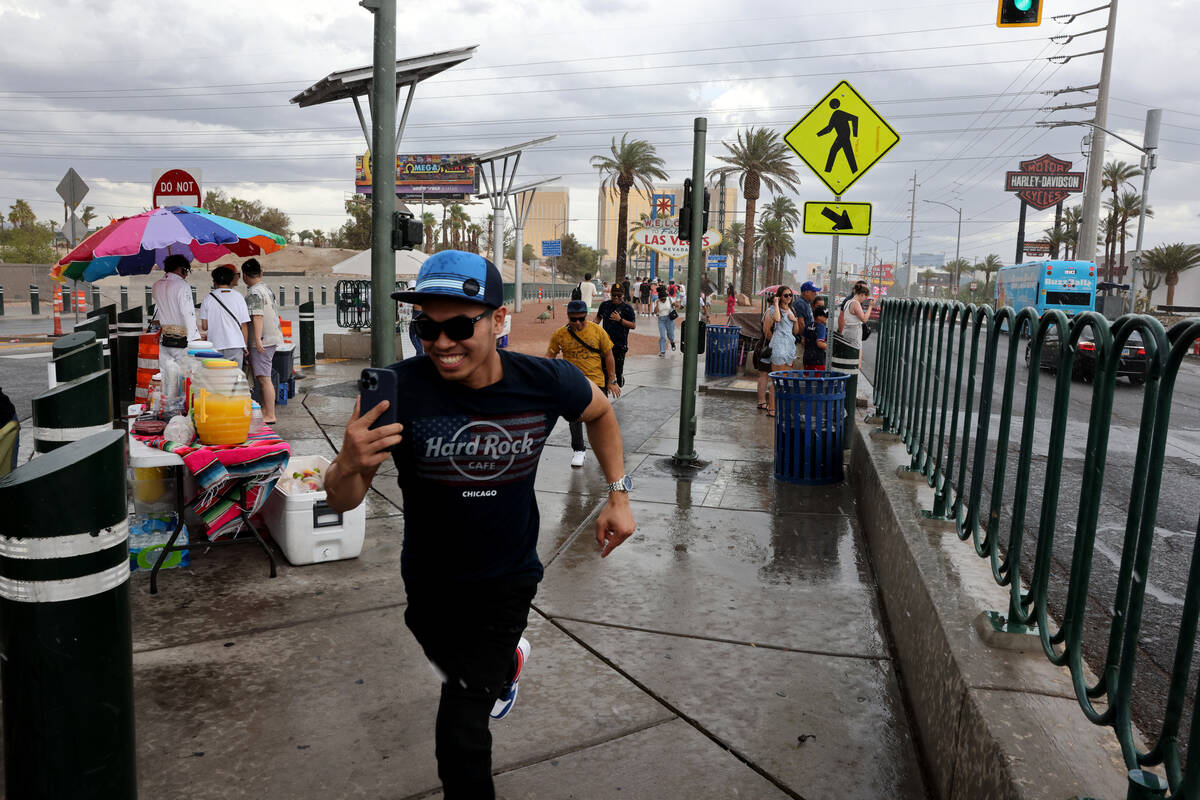 People run to their cars during a brief rainfall at the Welcome to Fabulous Las Vegas sign on t ...