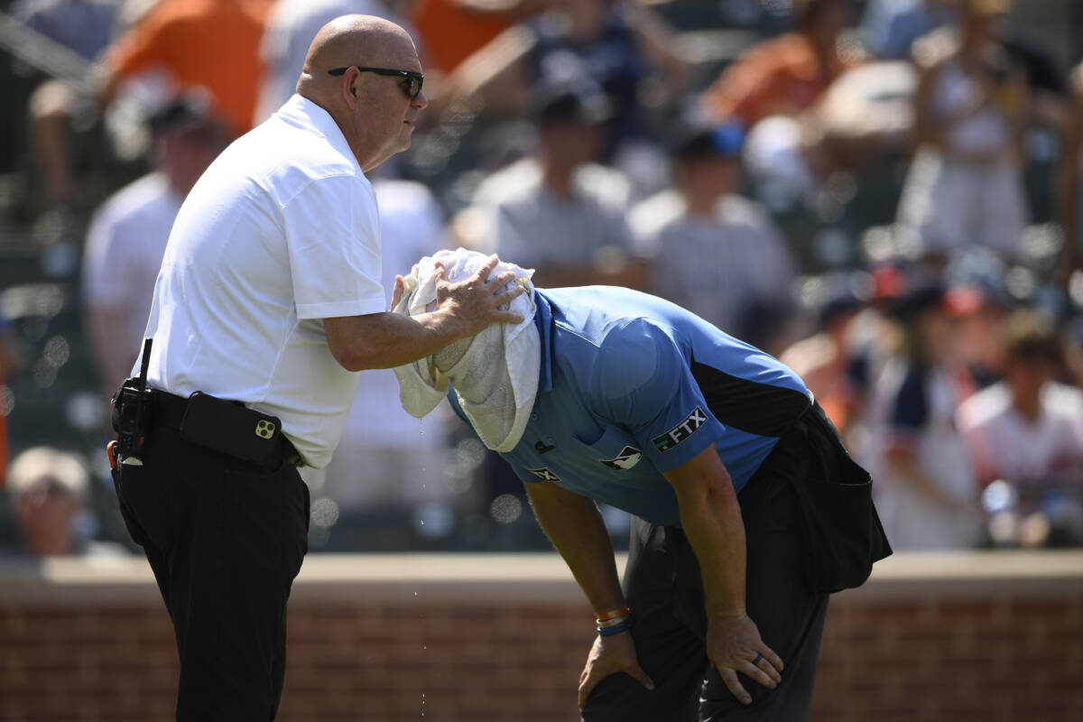 Baltimore Orioles head trainer Brian Ebel, left, helps home plate umpire Scott Barry get relief ...