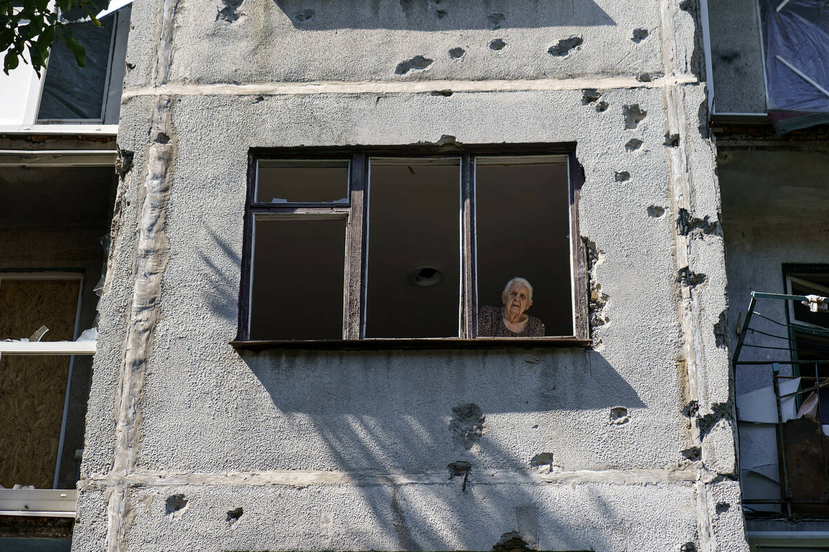 An elderly woman looks out of her apartment window in a damaged building from a May rocket atta ...