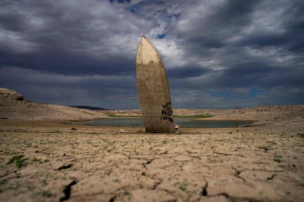 A formerly sunken boat stands upright into the air with its stern buried in the mud along the s ...