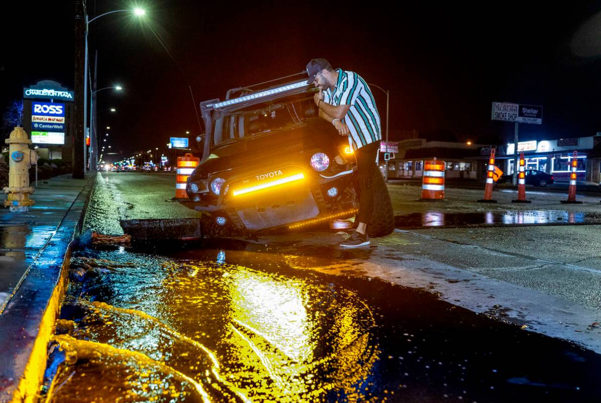 Driver Miguel Reyes checks out his vehicle stuck in a construction hole due to flooding along C ...