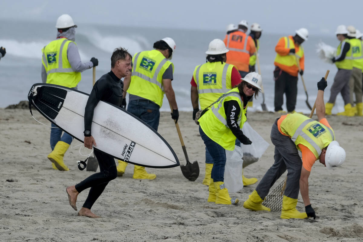 FILE - A surfer walks by as workers in protective suits continue to clean the contaminated beac ...