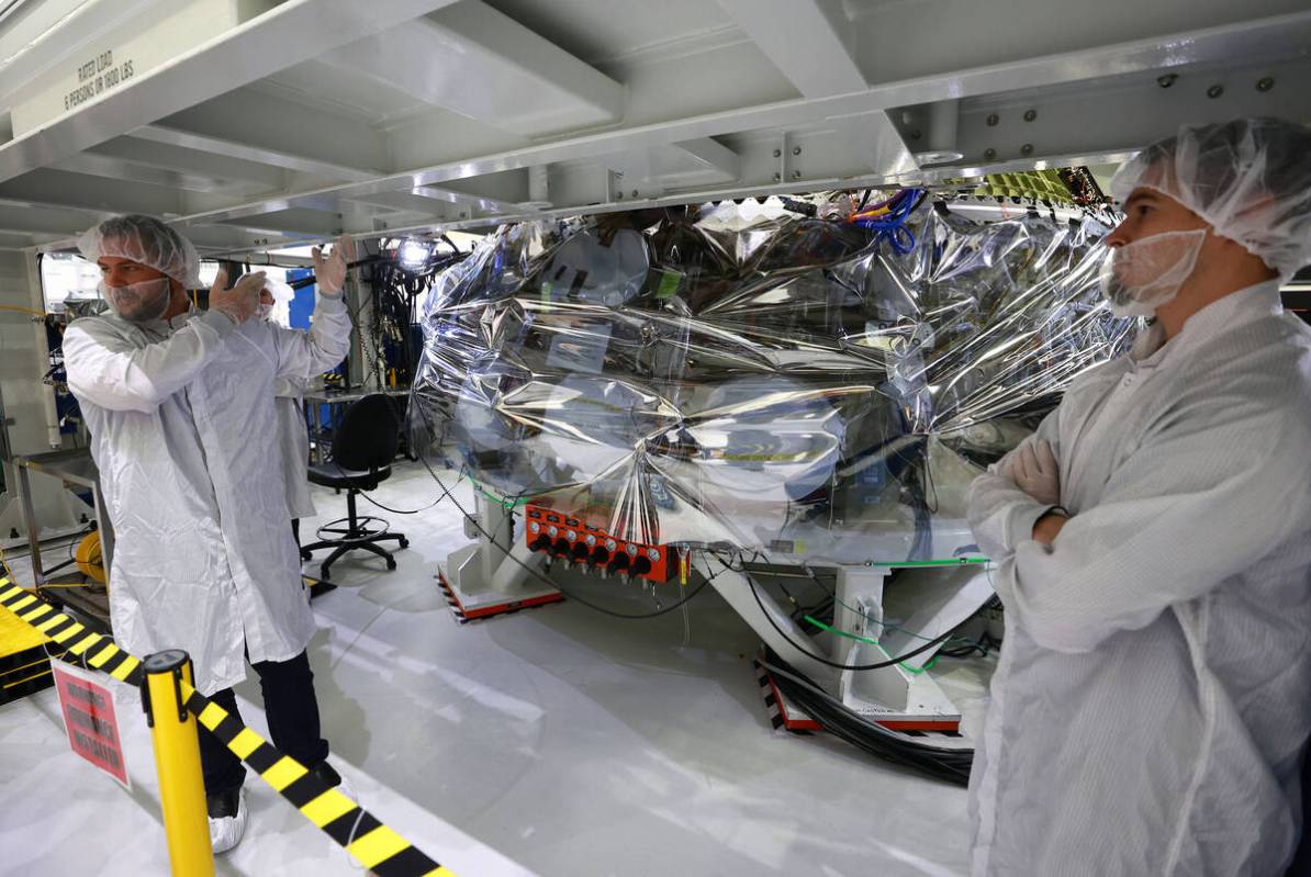 Orion program engineers talk in front of the Artemis II crew capsule being assembled at Kennedy ...