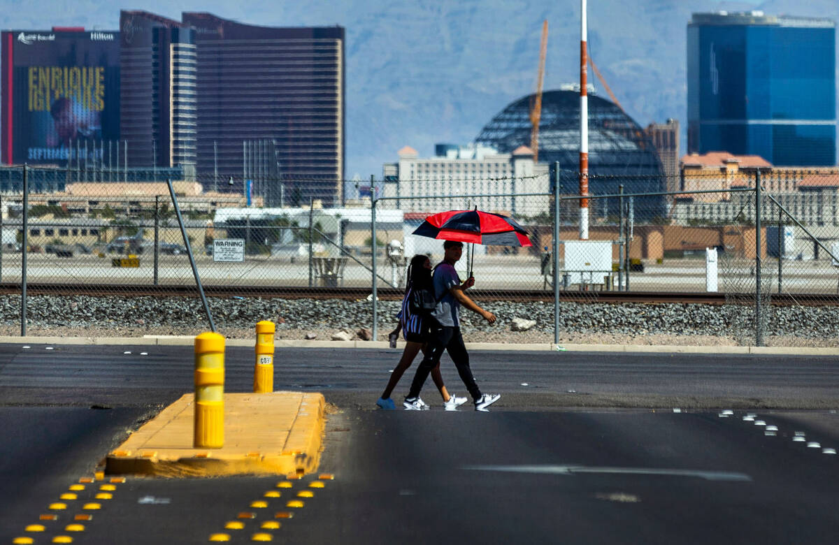 Laura Celtoro, left, and Reanaldo Revolta keep cool beneath an umbrella as they walk along East ...