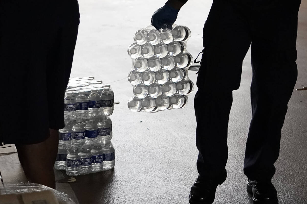 A recruit for the Jackson, Miss., Fire Department carries a case of bottled water to a resident ...