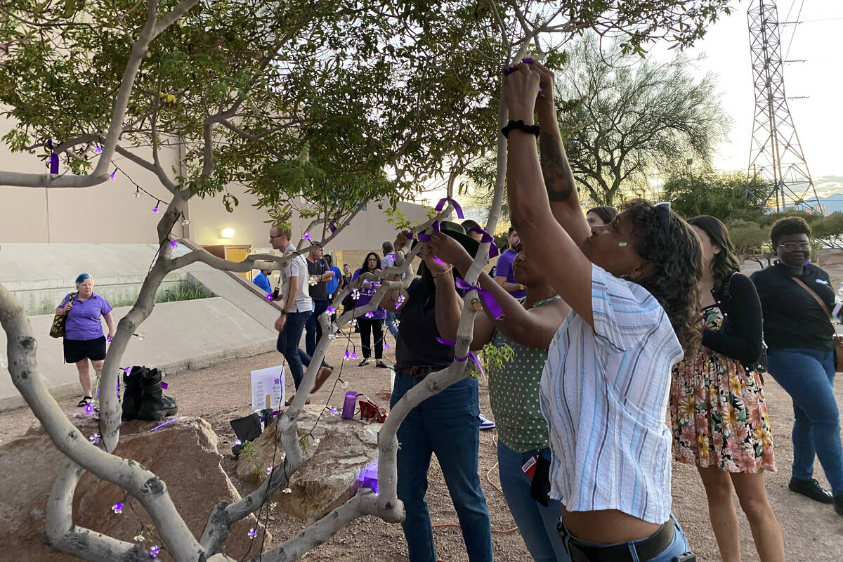 Sue Hanes reaches up to tie a purple ribbon on a tree in honor of those who have died from over ...