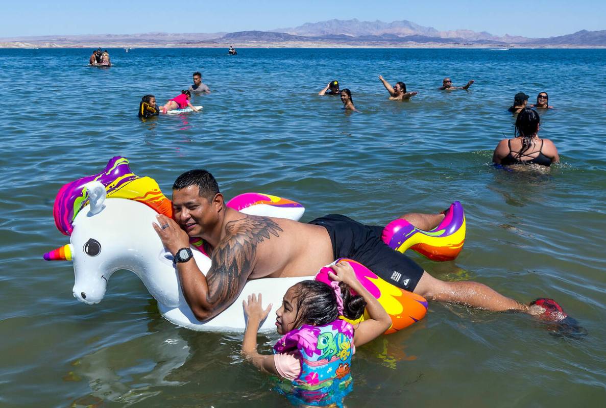 Jon Quenga relaxes atop of a unicorn float as Damari Evangelista, 8, hangs on along the shoreli ...