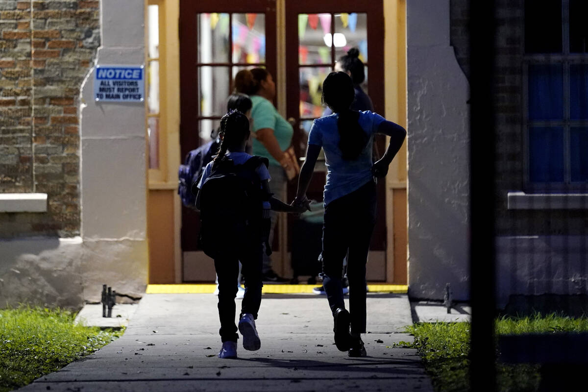 Students holds hands as they arrive at Uvalde Elementary, now protected by a fence and Texas St ...