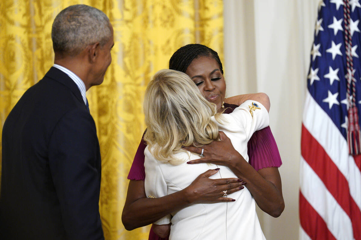 Former President Barack Obama looks on as former first lady Michelle Obama hugs first lady Jill ...