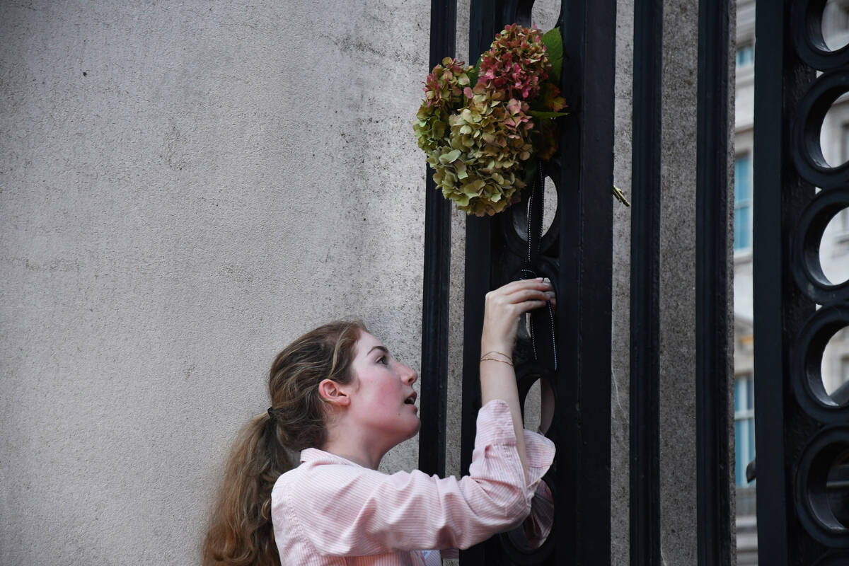 Christina Brask-Tyrell places an arrangement on a gate outside Buckingham Palace on Thursday, S ...