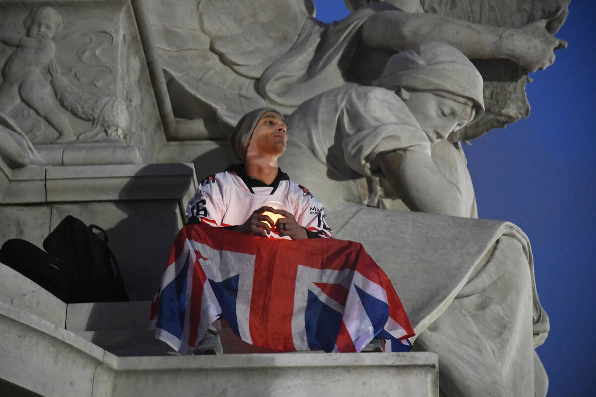 A mourner wrapped in the Union Jack flag, holds a light while ensconced on a monument outside B ...
