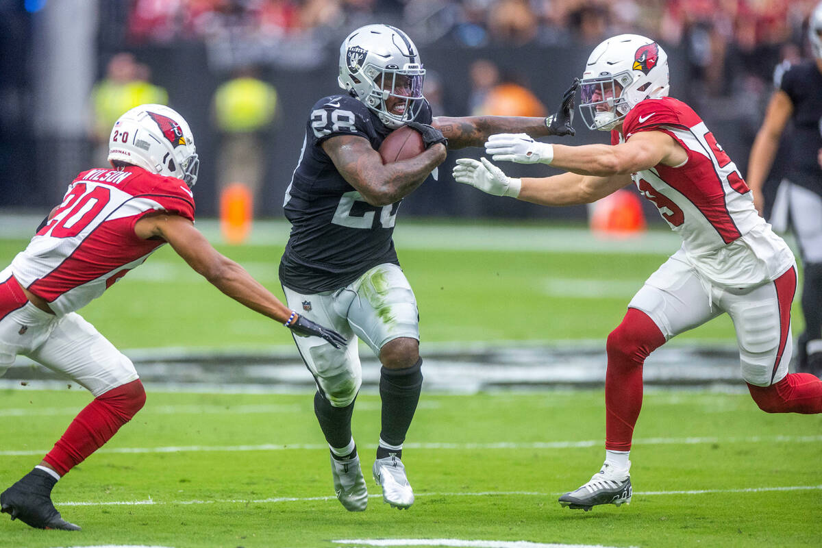 Raiders running back Josh Jacobs (28) splits the defense of Arizona Cardinals cornerback Marco ...