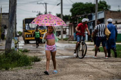 A youth uses an umbrella in Batabano, Cuba, Monday, Sept. 26, 2022. Hurricane Ian was growing s ...