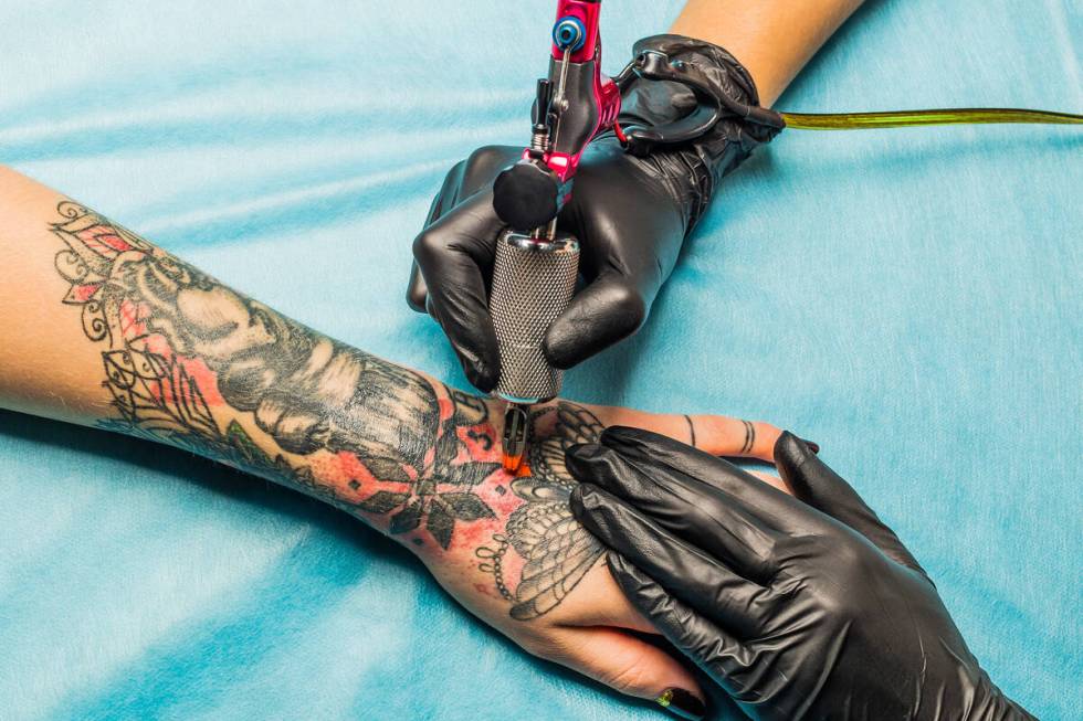 Close up tattoo artist demonstrates the process of getting black and red tattoo with orange pai ...