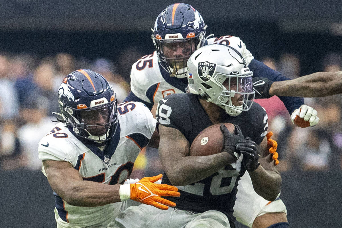 Raiders running back Josh Jacobs (28) tries to spin his way out of a tackle against Denver Bron ...