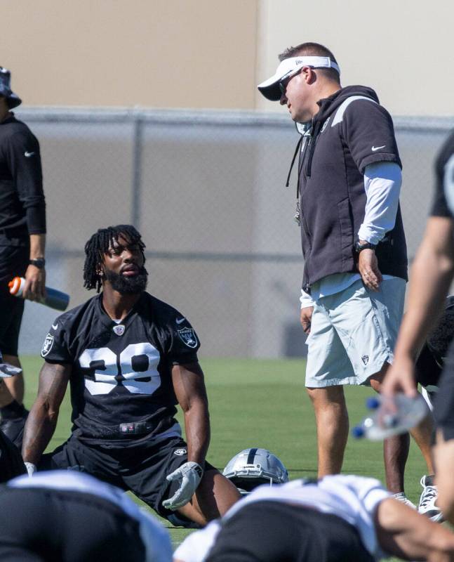 Raiders head coach Josh McDaniels speaks to Raiders cornerback Nate Hobbs (39) as he stretches ...