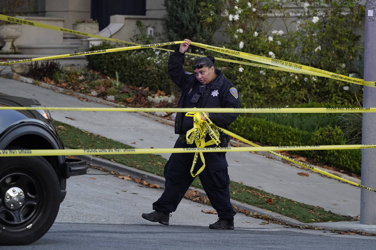 A police officer rolls out more yellow tape on the closed street below the home of Paul Pelosi, ...