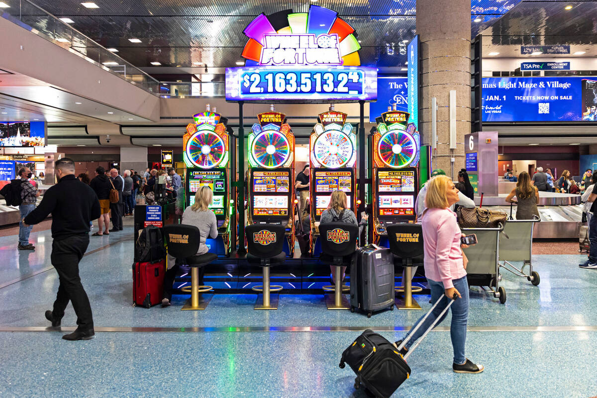 Travelers pass by slot machine players in the Terminal 1 baggage claim area at Harry Reid Inter ...