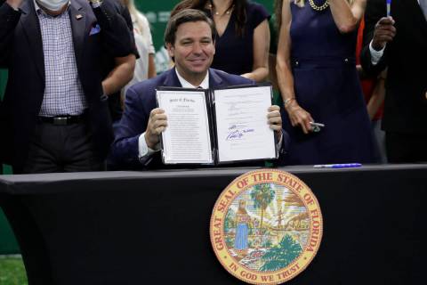 FILE - Florida Gov. Ron DeSantis holds up a just signed bill which would allow college athletes ...