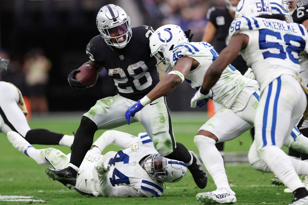 Raiders running back Josh Jacobs (28) runs the ball under pressure from Indianapolis Colts line ...