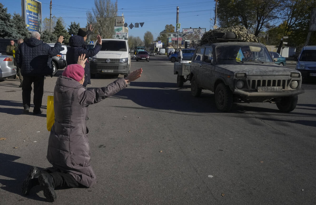 A woman kneels on the ground in front of passing Ukrainian Army car in Kherson, Ukraine, Tuesda ...