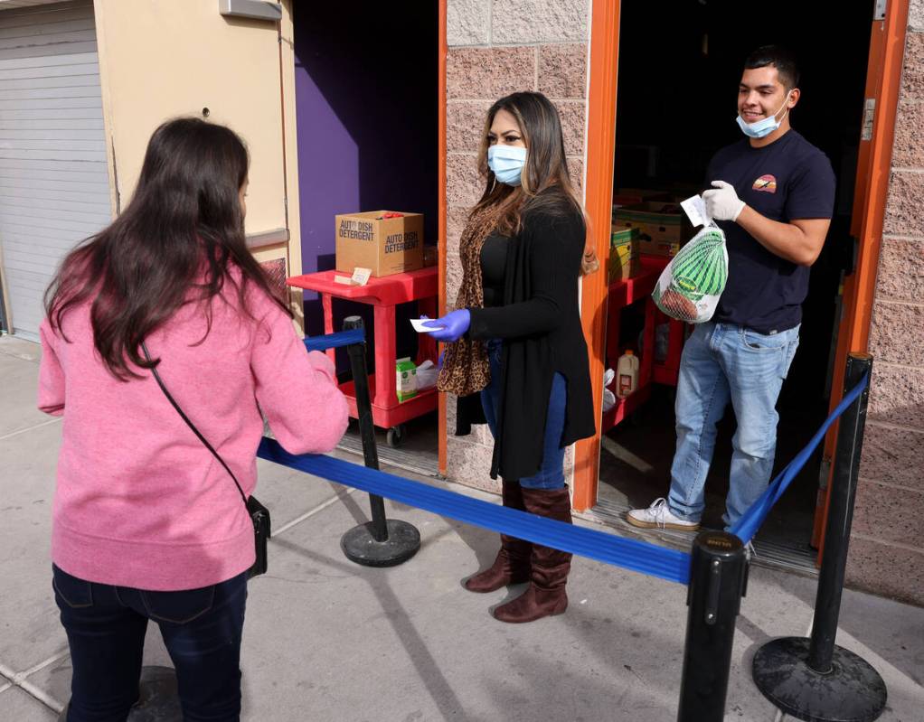 Maria Ochoa, center, and Randy Flores give a turkey and other food to a client at the Hands of ...