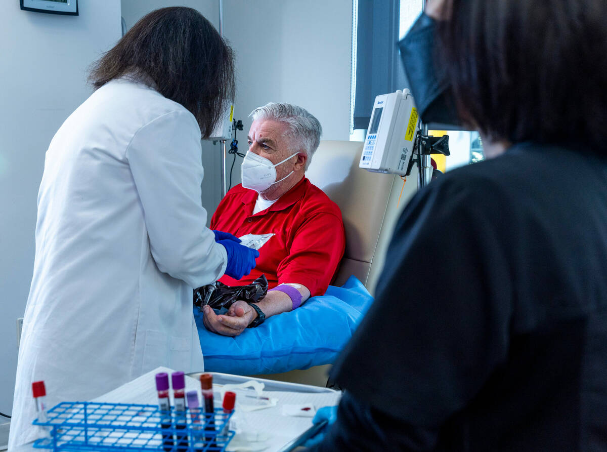 Clinical trial participant Bob Lathrop, center, sits comfortably as infusion room RN Betty Rome ...